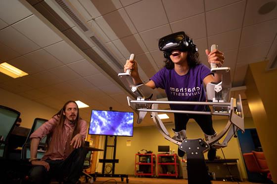 图为一名冰球突破app的学生在沉浸式媒体实验室的虚拟现实机器里, while a professor watches