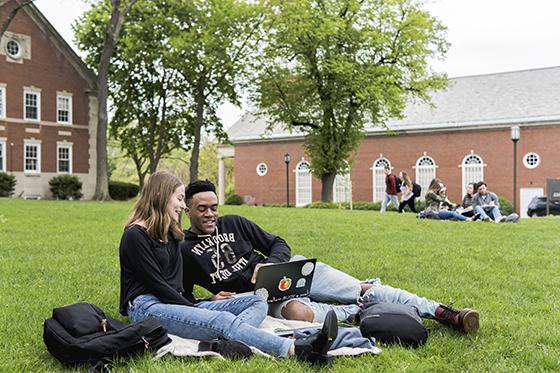 两名冰球突破app的学生坐在绿草地上的学术广场上，一起用笔记本电脑工作. 