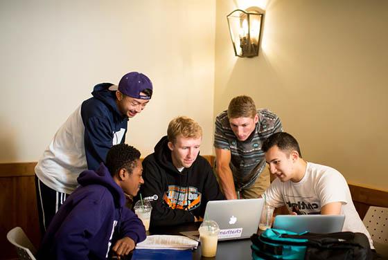 图为一群冰球突破app的男学生围着几台笔记本电脑一起工作