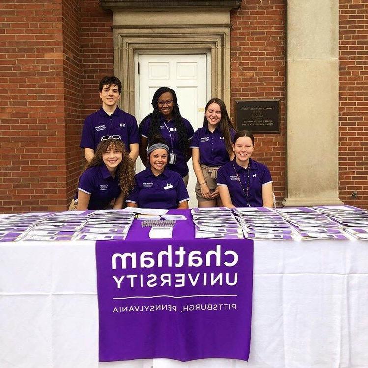 Photo of six Chatham University students in purple shirts, working at a table outside on 冰球突破mg登录网址
