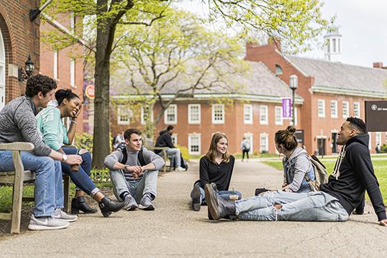 图为六名冰球突破app学生坐在红砖教学楼外的地上和长椅上聊天