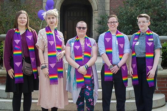 图为一群英国冰球突破app的学生穿着印有彩虹LGBTQ+图案的毕业礼服, posing together for a photo. 